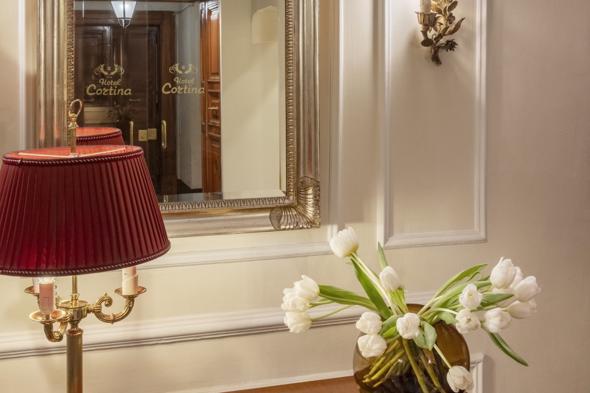 Close-up detail in the lobby of Hotel Cortina in Rome, showcasing an antique mirror reflecting the engraved Hotel Cortina logo and a classical lamp - Hotel Cortina, BZAR hotels in Rome