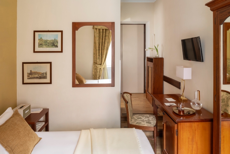 Serene view of a Small room at Hotel Cortina in Rome, featuring a master single bed, brown velvet pillows, an antique wooden wardrobe, and a large window with patterned and sheer curtains - Hotel Cortina, BZAR hotels in Rome