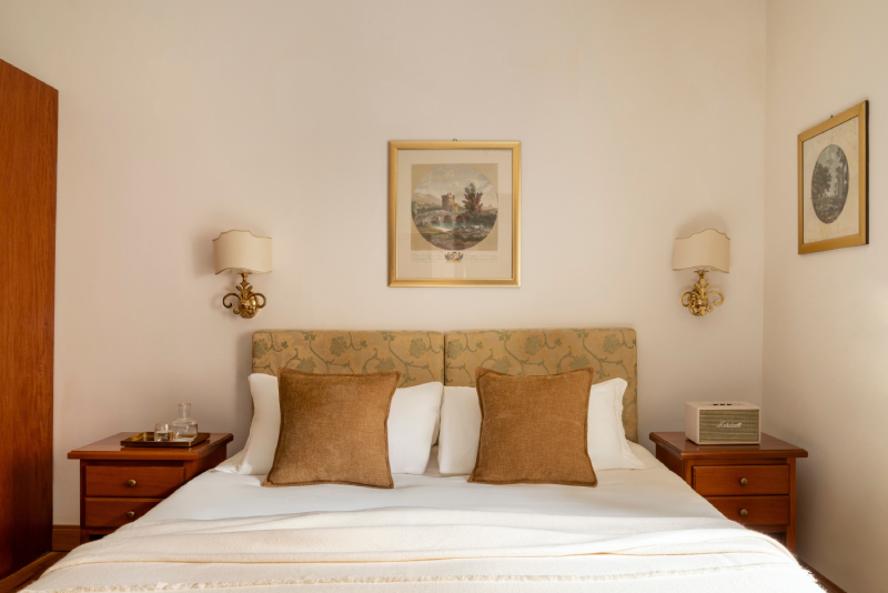 Detail of the double bed in a standard room at Hotel Cortina in Rome, showing a patterned headboard, two brown velvet pillows, and two antique nightstands with matching lamps - Hotel Cortina, BZAR hotels in Rome