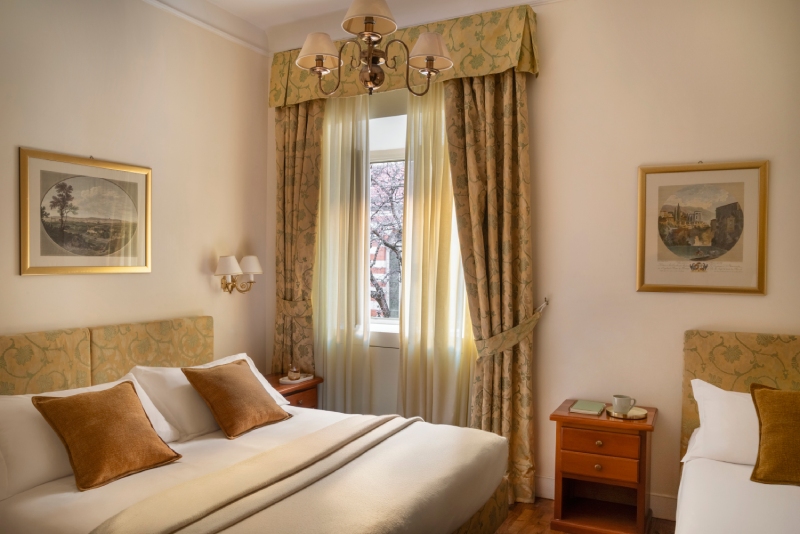 Spacious triple room at Hotel Cortina in Rome, featuring a double bed and a separate single bed, decorated in a classic style with wooden floors, antique framed art, and a bright central window - Hotel Cortina, BZAR hotels in Rome